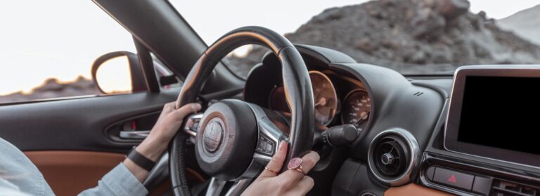 Frau fährt Auto auf der Wüstenstraße, Nahaufnahme mit Fokus auf das Lenkrad und die Hände