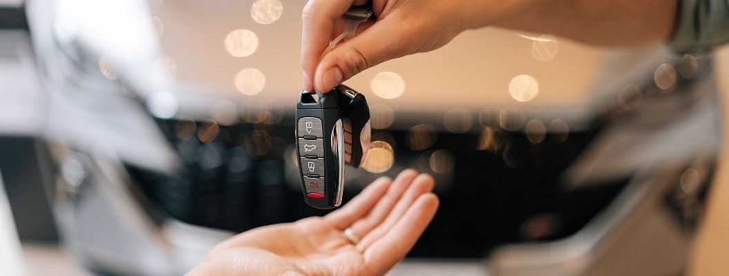 Nahaufnahme der Hände eines nicht erkennbaren männlichen Händlers, der einem Kunden den Schlüssel für ein neues Auto übergibt, vor einem unscharfen Hintergrund eines neuen Autos im Büro des Händlers.